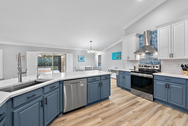 kitchen featuring blue cabinets, white cabinets, hanging light fixtures, stainless steel appliances, and wall chimney range hood