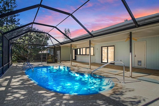 pool at dusk with ceiling fan, a patio area, and glass enclosure