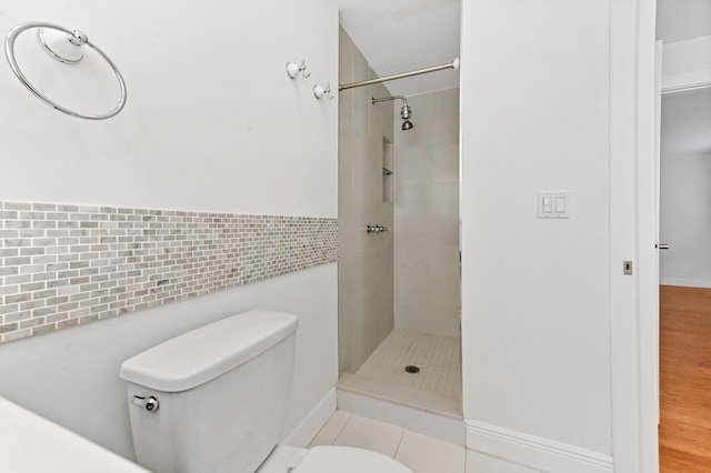 bathroom with tile patterned flooring, a tile shower, toilet, and tile walls