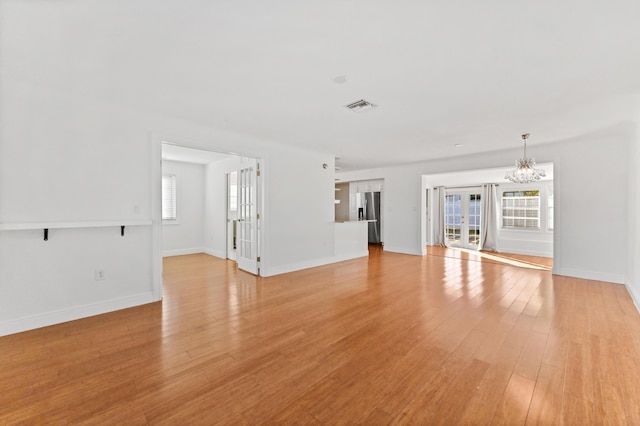 unfurnished living room with light hardwood / wood-style floors, an inviting chandelier, and a wealth of natural light