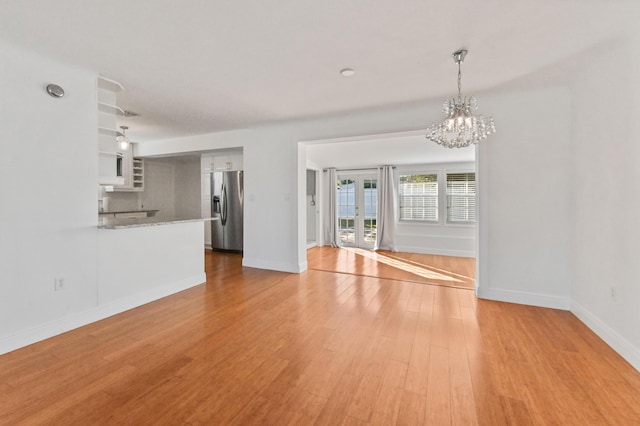 unfurnished living room featuring an inviting chandelier and light wood-type flooring