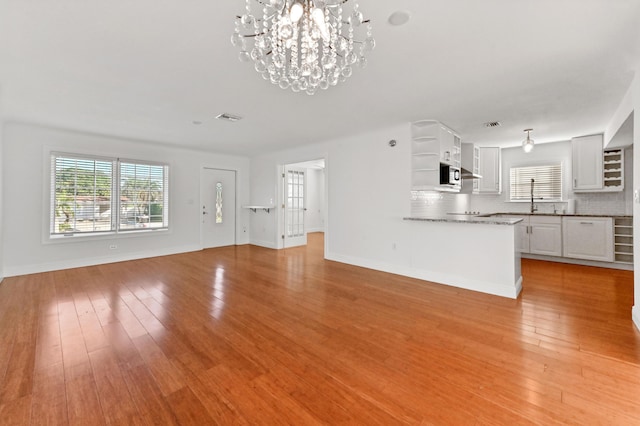 unfurnished living room featuring a notable chandelier, light wood-type flooring, and sink