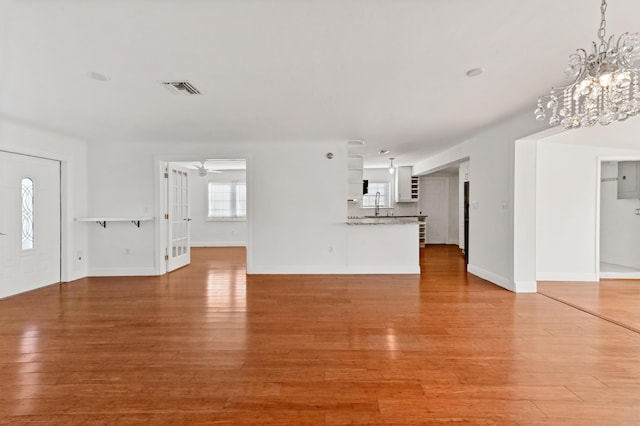 unfurnished living room featuring hardwood / wood-style flooring, ceiling fan with notable chandelier, and sink