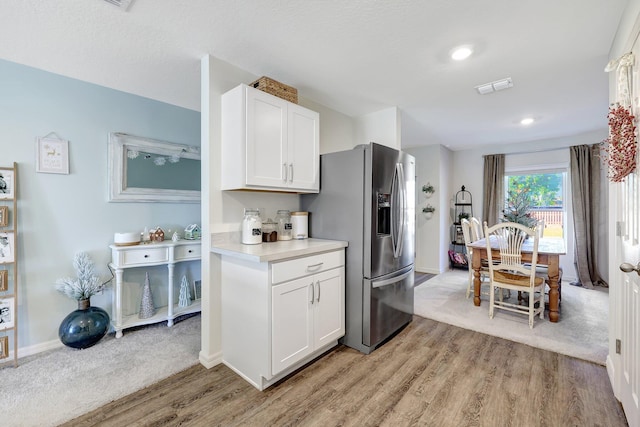 kitchen with stainless steel fridge, white cabinetry, and light hardwood / wood-style flooring