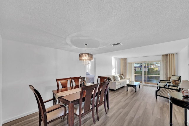 dining room with light hardwood / wood-style flooring, a chandelier, and a textured ceiling