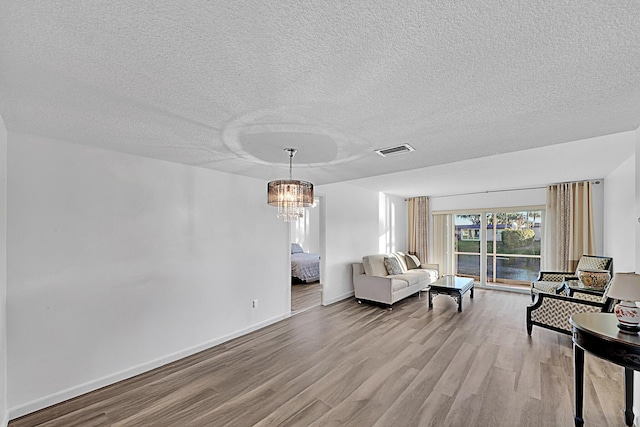 living room featuring light hardwood / wood-style floors, a textured ceiling, and a notable chandelier