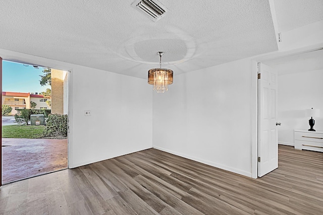 unfurnished room featuring an inviting chandelier, hardwood / wood-style flooring, and a textured ceiling