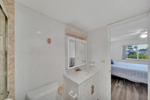 bathroom with wood-type flooring, tile walls, vanity, ceiling fan, and toilet