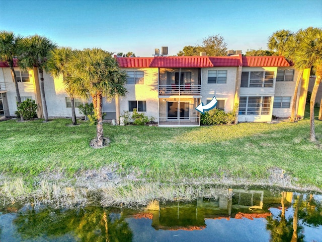 rear view of property with a yard, a water view, and a balcony