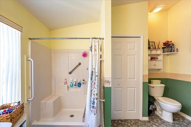 bathroom with a shower with shower curtain, plenty of natural light, toilet, and lofted ceiling