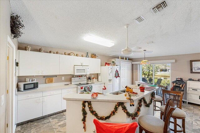 kitchen featuring a textured ceiling, white cabinets, decorative light fixtures, and white appliances