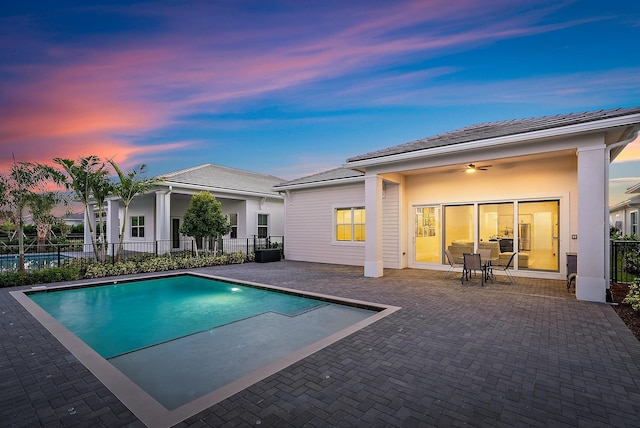 pool at dusk with a patio and ceiling fan