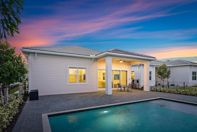 back house at dusk with a patio area, a fenced in pool, and ceiling fan