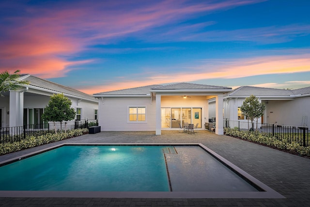 pool at dusk with a patio and ceiling fan