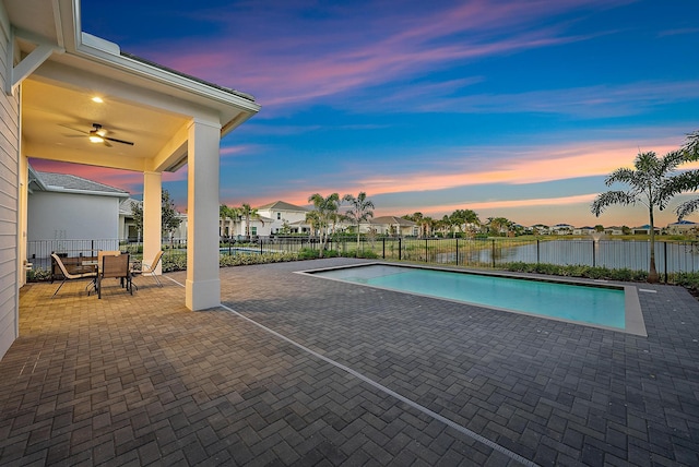 pool at dusk featuring ceiling fan and a patio