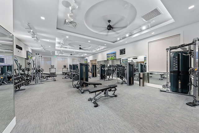 gym with ceiling fan, carpet flooring, and a tray ceiling