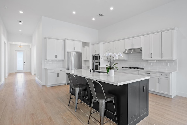 kitchen featuring appliances with stainless steel finishes, white cabinetry, an island with sink, decorative backsplash, and a breakfast bar area