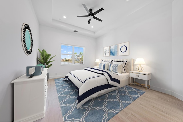 bedroom featuring light hardwood / wood-style floors, a tray ceiling, and ceiling fan