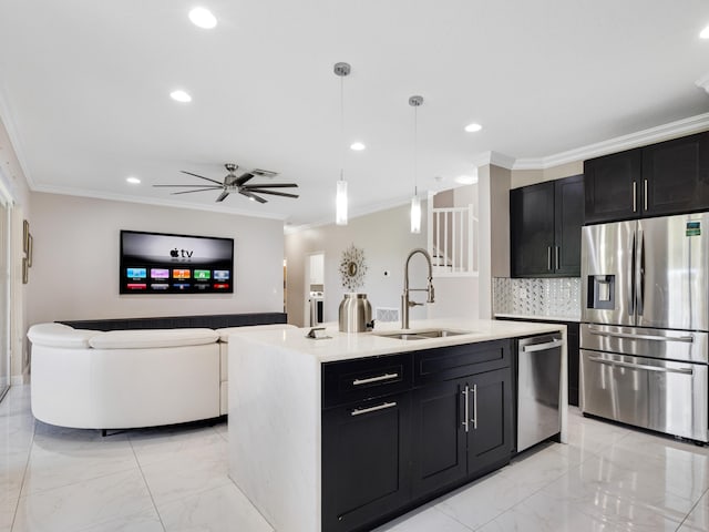 kitchen featuring sink, hanging light fixtures, ornamental molding, stainless steel appliances, and a center island with sink