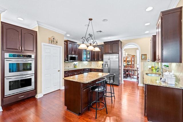 kitchen featuring pendant lighting, a center island, appliances with stainless steel finishes, tasteful backsplash, and dark hardwood / wood-style flooring