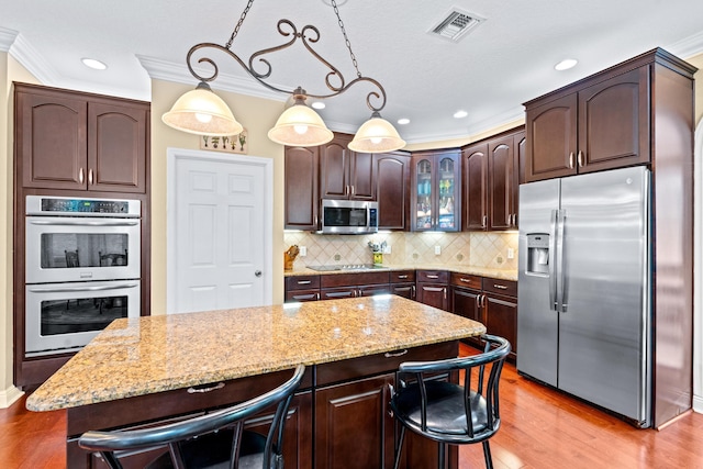 kitchen featuring a kitchen breakfast bar, hanging light fixtures, dark brown cabinets, a kitchen island, and stainless steel appliances