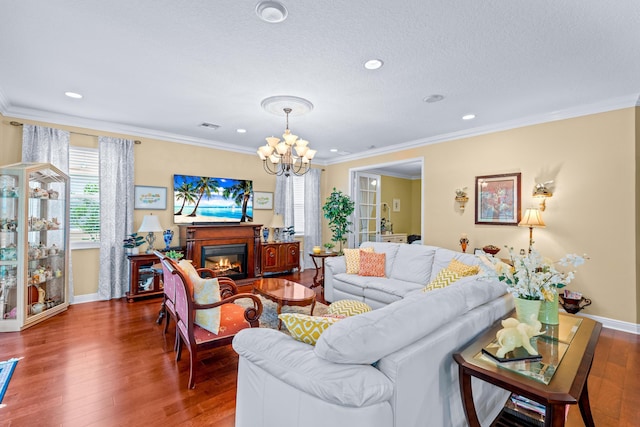 living room featuring wood-type flooring, a textured ceiling, ornamental molding, and a notable chandelier