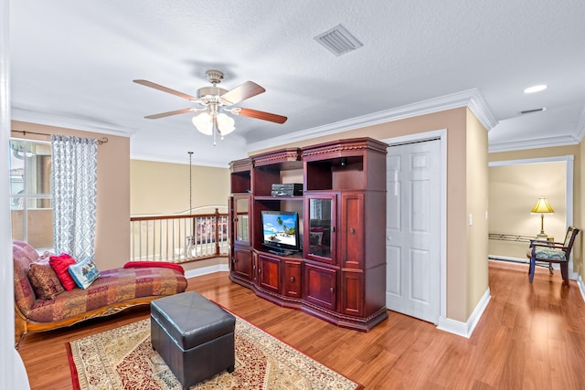 living room featuring ceiling fan, ornamental molding, a textured ceiling, and light hardwood / wood-style flooring