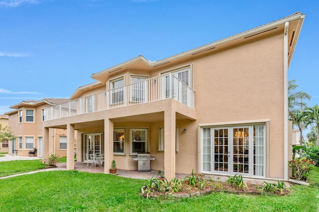 back of property featuring french doors, a balcony, a patio area, and a lawn