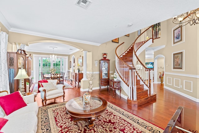 living room with decorative columns, a chandelier, wood-type flooring, and ornamental molding