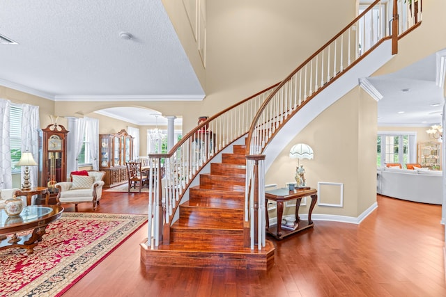 stairway featuring ornate columns, wood-type flooring, a textured ceiling, and ornamental molding