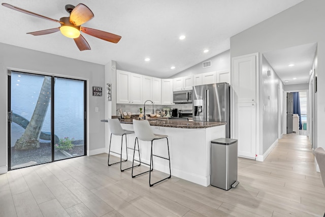 kitchen with ceiling fan, kitchen peninsula, vaulted ceiling, white cabinets, and appliances with stainless steel finishes