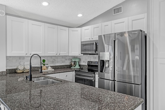 kitchen featuring appliances with stainless steel finishes, vaulted ceiling, white cabinetry, and dark stone countertops