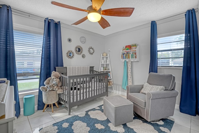 tiled bedroom with multiple windows, ceiling fan, a nursery area, and a textured ceiling