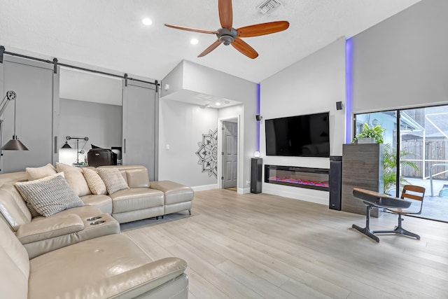 living room featuring a barn door, light hardwood / wood-style floors, high vaulted ceiling, and ceiling fan