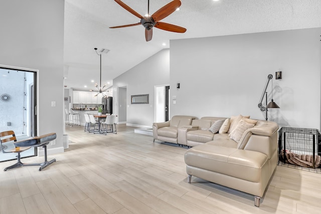 living room featuring ceiling fan with notable chandelier, light hardwood / wood-style floors, a textured ceiling, and high vaulted ceiling