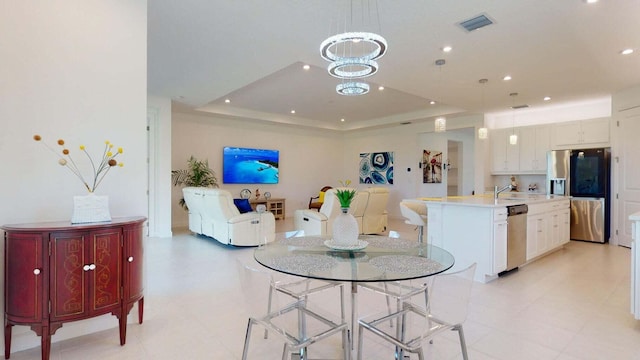 dining space featuring a raised ceiling, sink, and a notable chandelier