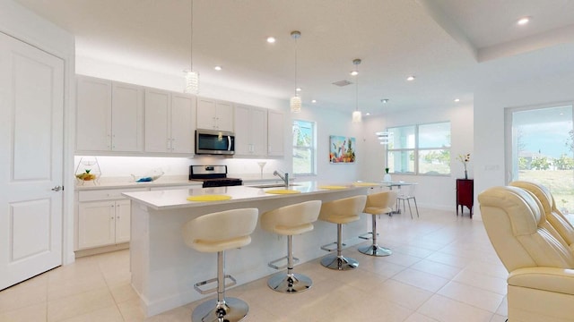 kitchen with a center island with sink, sink, stainless steel appliances, and hanging light fixtures