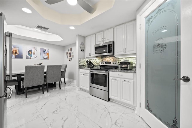 kitchen featuring ceiling fan, a raised ceiling, decorative backsplash, white cabinets, and appliances with stainless steel finishes