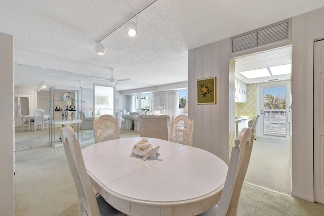 carpeted dining room with a textured ceiling, track lighting, plenty of natural light, and ceiling fan