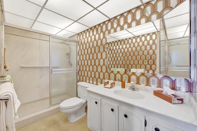 bathroom with a drop ceiling, vanity, a shower with shower door, and toilet