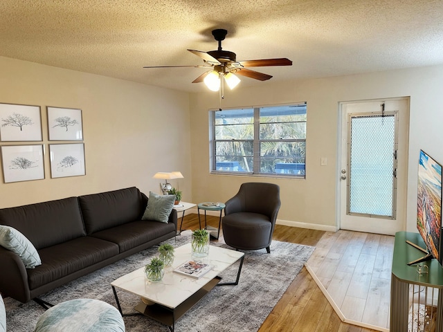 living area featuring baseboards, a textured ceiling, a ceiling fan, and wood finished floors