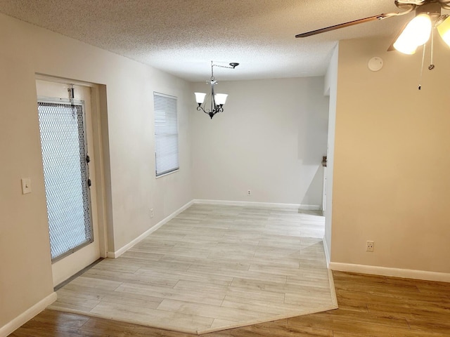 unfurnished dining area with light hardwood / wood-style flooring, ceiling fan with notable chandelier, and a textured ceiling