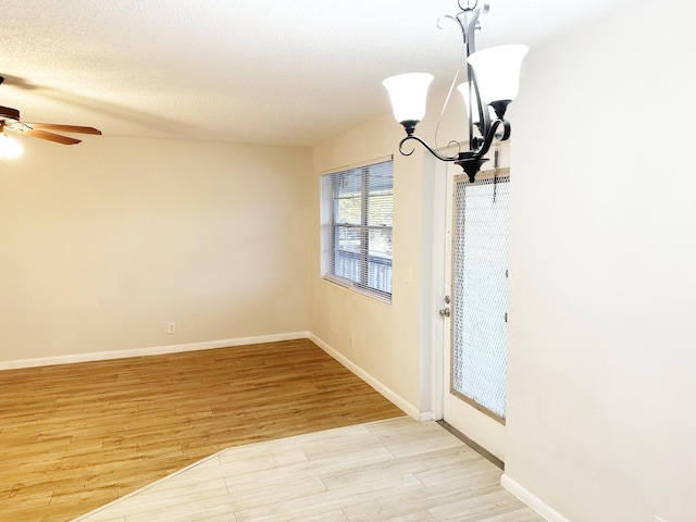 unfurnished dining area featuring a textured ceiling, ceiling fan with notable chandelier, and light hardwood / wood-style floors