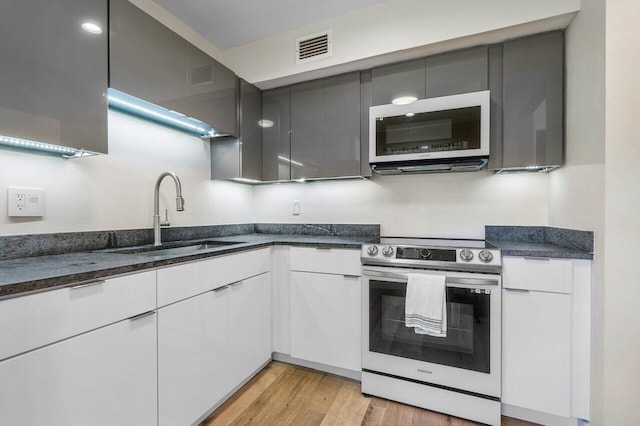 kitchen with electric stove, sink, white cabinets, and light hardwood / wood-style floors