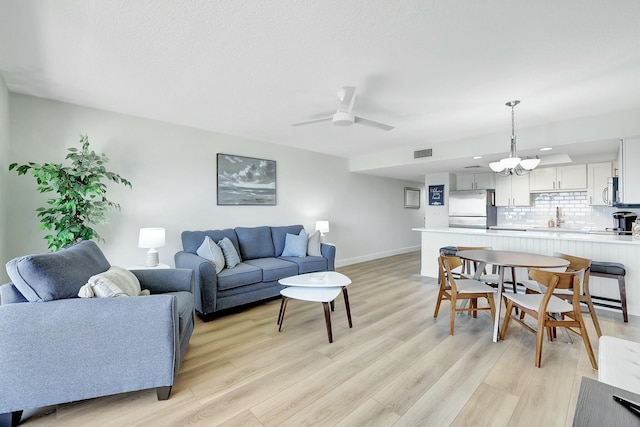 living room featuring ceiling fan with notable chandelier and light wood-type flooring