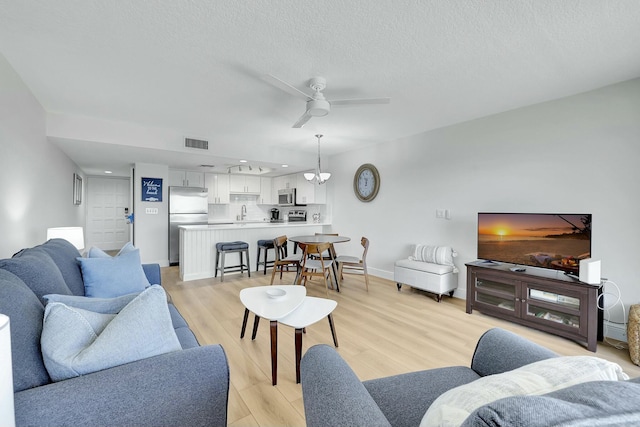 living room featuring ceiling fan, sink, a textured ceiling, and light wood-type flooring