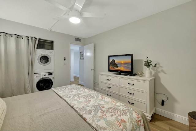 bedroom featuring ceiling fan, stacked washer and dryer, and light hardwood / wood-style floors