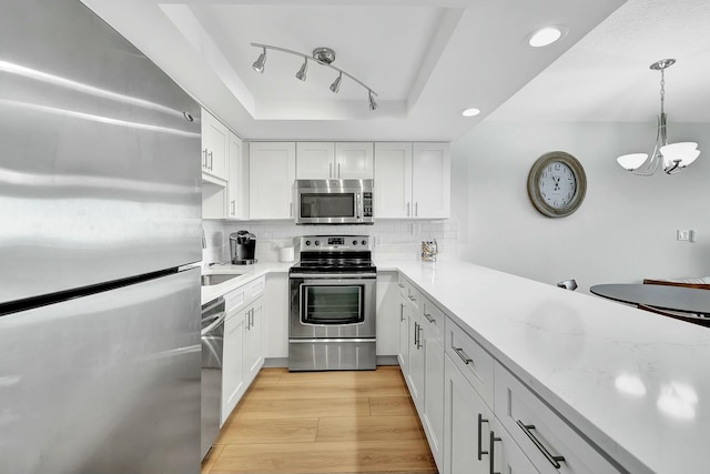 kitchen with backsplash, stainless steel appliances, light hardwood / wood-style floors, white cabinetry, and hanging light fixtures