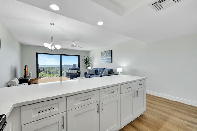 kitchen featuring white cabinets, ceiling fan with notable chandelier, hanging light fixtures, light wood-type flooring, and light stone counters