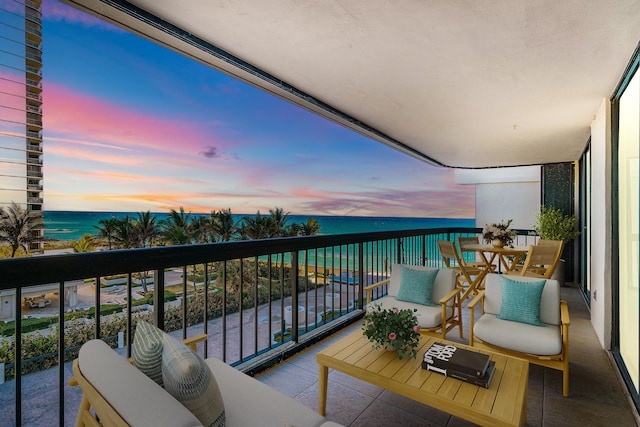 balcony at dusk with a water view and a view of the beach